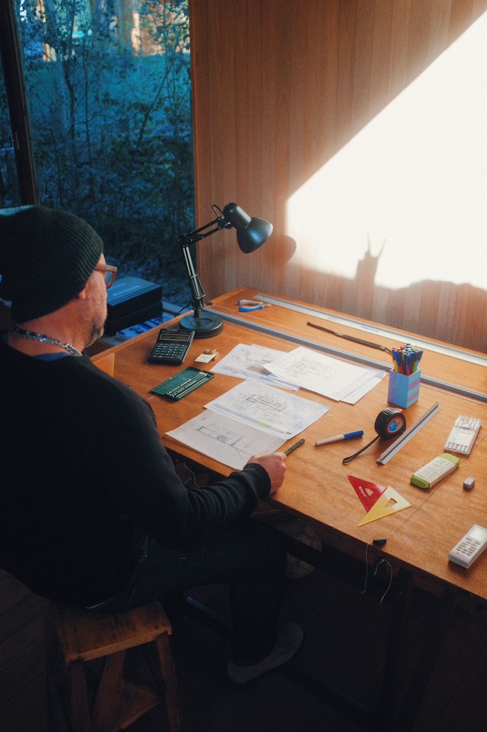 Arkitekt som jobber med tegninger ved et solbelyst tegnebord.